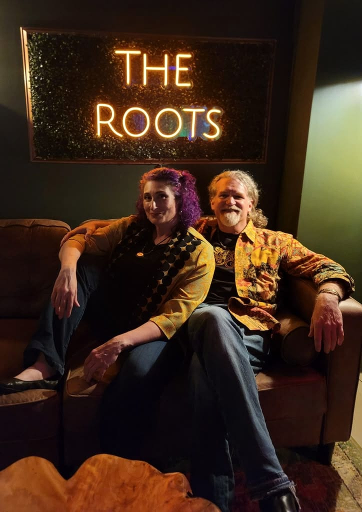 Kristi and Steven on the couch beneath the neon sign at The Roots